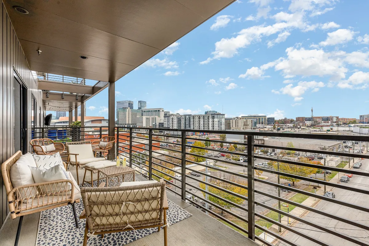 A contemporary balcony space with comfortable seating overlooks the city skyline. Decorative rugs and modern furnishings create a relaxed yet upscale vibe, ideal for unwinding after a busy day or hosting casual team gatherings. The cityscape stretches out beyond the balcony, visually connecting the property to Nashville’s downtown environment.