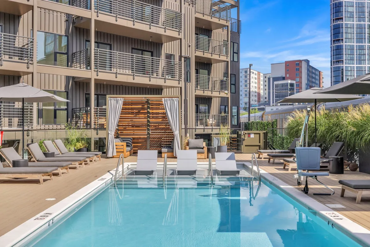 A sparkling swimming pool surrounded by lounge chairs and umbrellas, with a modern building as the backdrop. The scene is lively yet relaxed, ideal for sunbathing, poolside socializing, or unwinding between city adventures.