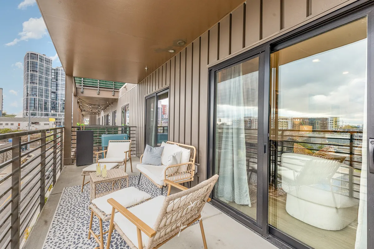 This exterior image showcases an inviting rooftop seating area adorned with a decorative rug and contemporary outdoor furniture, all set against an impressive city skyline backdrop. The space exudes a tranquil, sociable vibe, perfect for group gatherings, toasts, or relaxed morning coffees with a view.