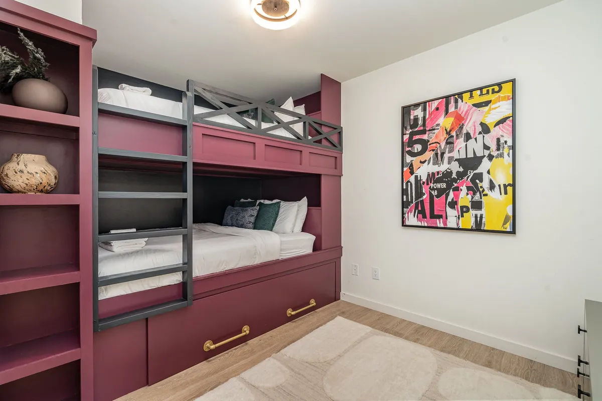 A cheerful bunk room featuring a queen-over-queen bunk bed accented by colorful artwork and playful décor. The space is bright and designed to accommodate families or groups, with a shelf for books and decorative items.