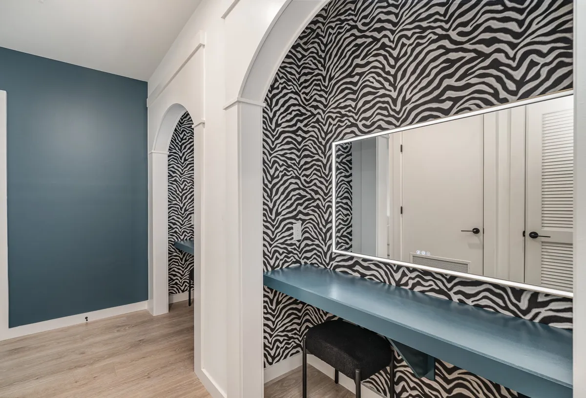 A lively and vibrant entry space with zebra-patterned wallpaper, large mirror, blue vanity table, and arched doorways. The scene captures the energy of getting ready or managing arrivals for special occasions.