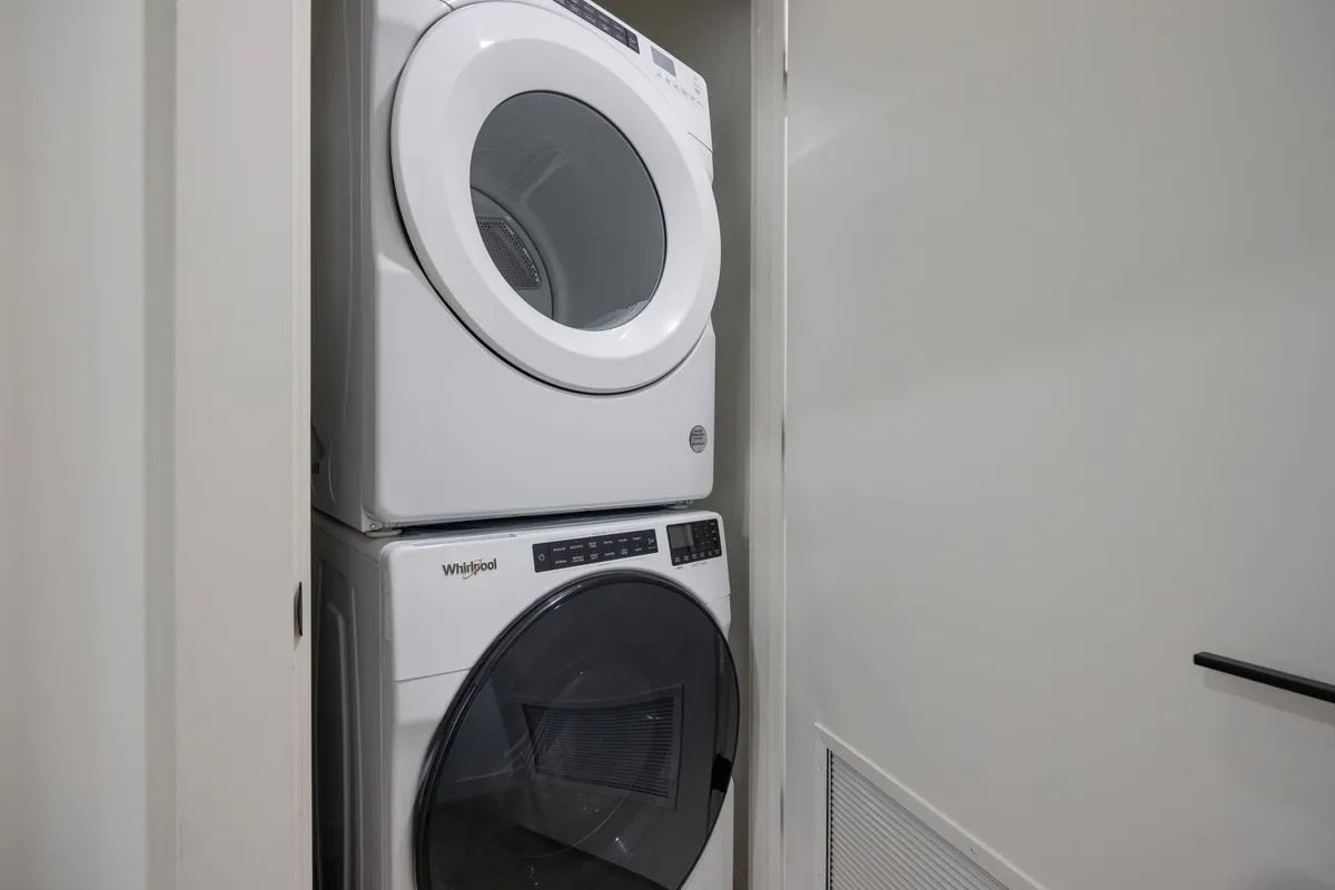 A compact laundry area featuring a stacked washer and dryer against clean white walls, conveying efficiency and utility for guests to handle laundry needs.