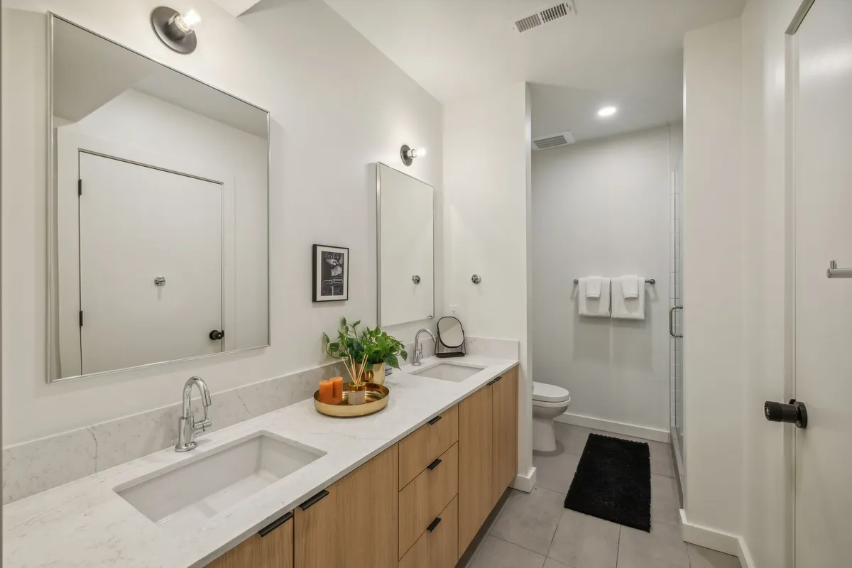 A spa-inspired bathroom with double sinks, modern mirrors, wood cabinetry, soft towels, and decorative plants, creating an atmosphere of calm and indulgence. The layout is both functional and soothing, ideal for self-care routines.