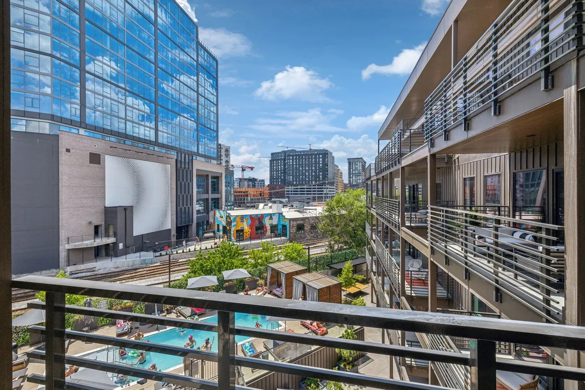A lively pool area featuring a sparkling swimming pool, modern buildings, a colorful mural, and inviting lounge spaces. The space is ideal for socializing, sunbathing, or playing outdoor games—a perfect retreat after a day exploring the city.