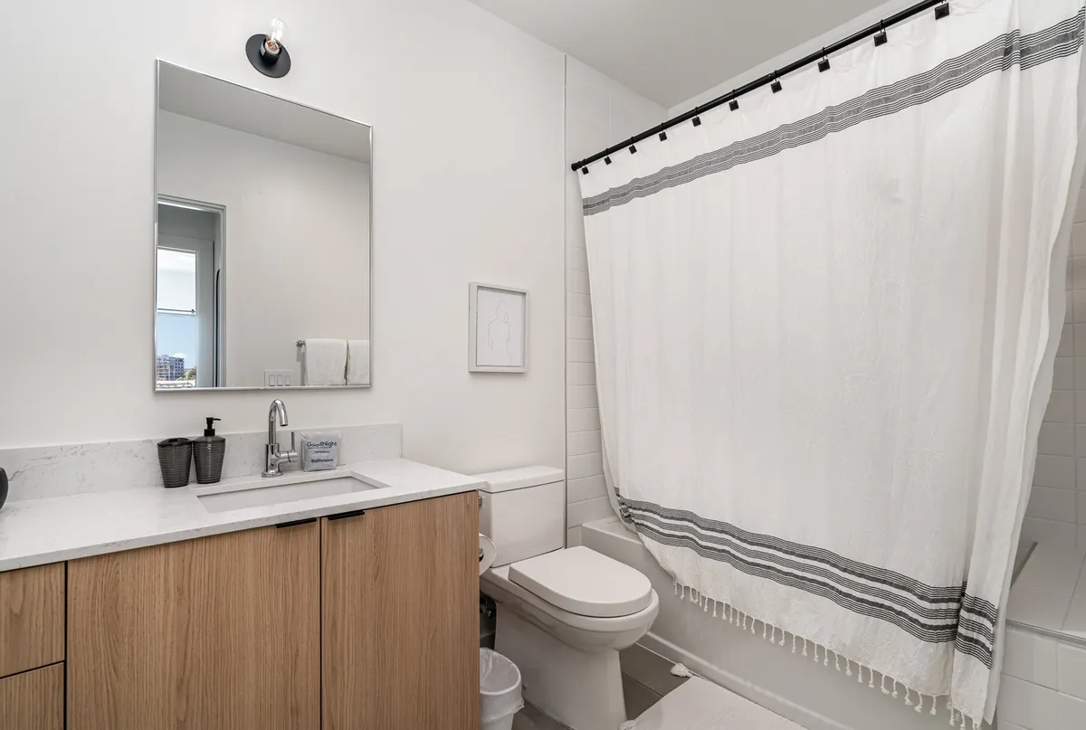 A fresh and inviting bathroom with a large mirror, modern sink, shower curtain, and wood cabinetry. The space feels bright and clean, suggesting attention to detail and comfort for guests’ morning routines.