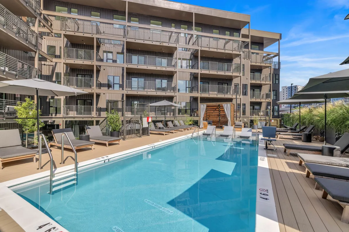 This image showcases a sparkling swimming pool surrounded by lounge chairs and balconies, with landscaped greenery providing a tranquil backdrop. The pool area is inviting, perfect for both relaxation and social gatherings. The building's modern facade and the communal layout highlight a family-friendly environment.