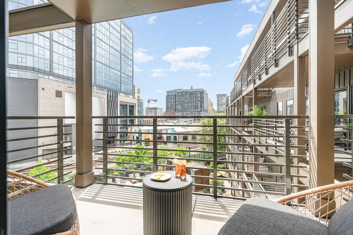 A stylish balcony setup overlooking the dazzling city skyline, with comfortable seating and refreshments on the table. The scene suggests unwinding with friends after a night out, enjoying the city lights, or preparing for another evening of adventure.